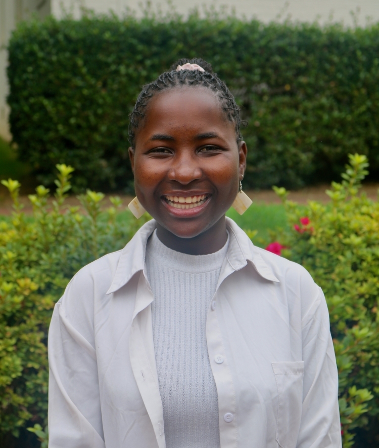 a young woman with dark hair wearing gold earrings and a white top smiling outside