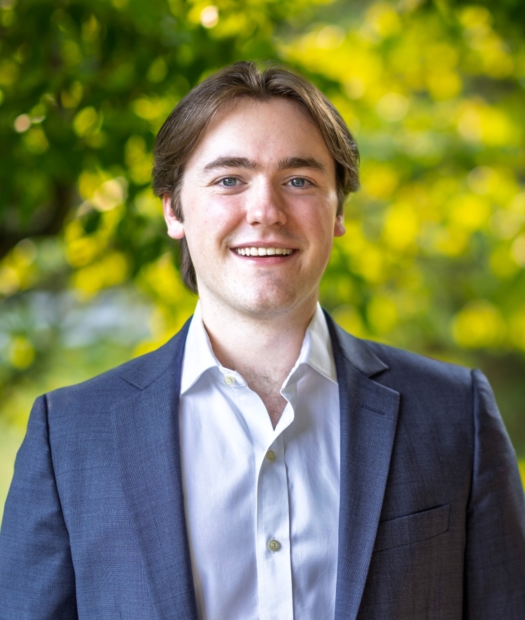 a young white man with short brown hair wearing a collared shirt and blue blazer