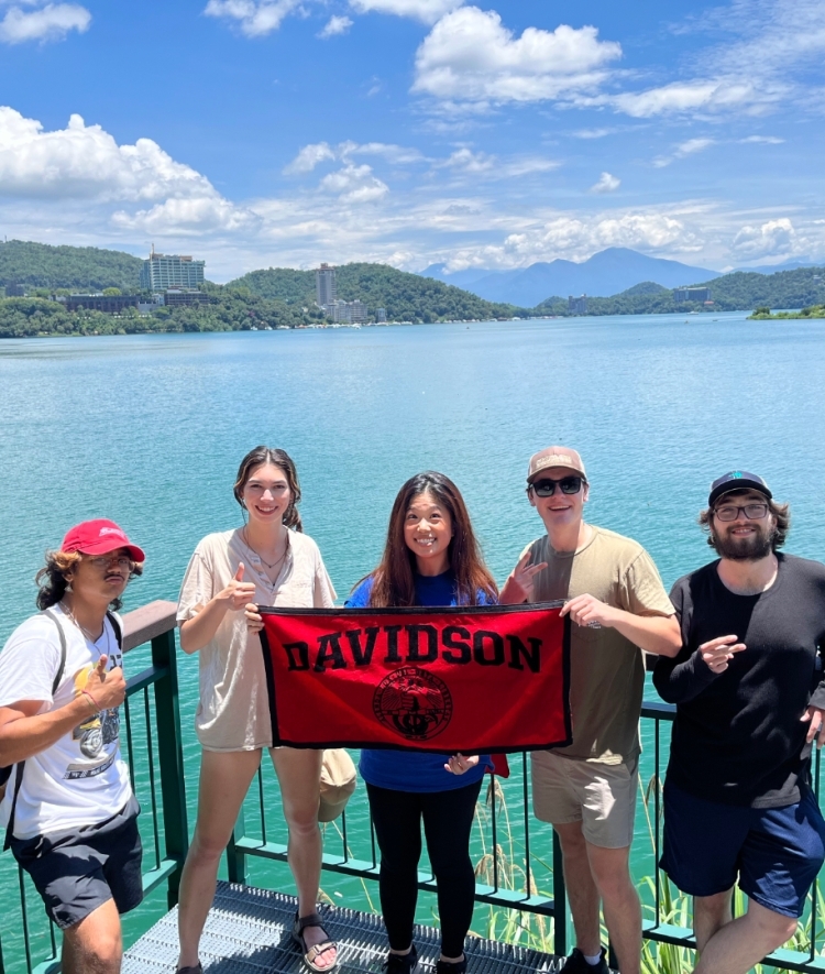 a group of young people smiling in front of water holding a "Davidson College" banner