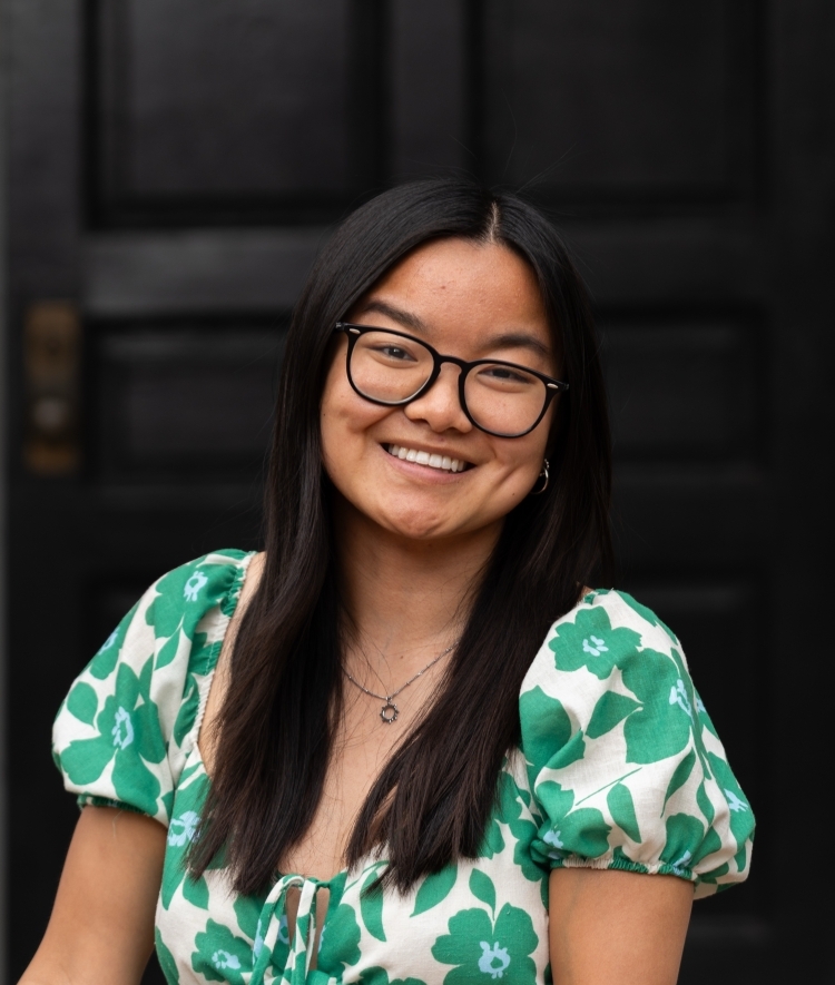 a young woman with black hair and glasses smiling wearing a green and white floral dress