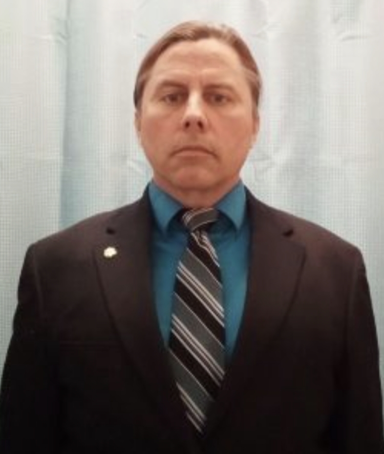 Man with dark hair wearing suit, deep teal button down shirt and striped tie