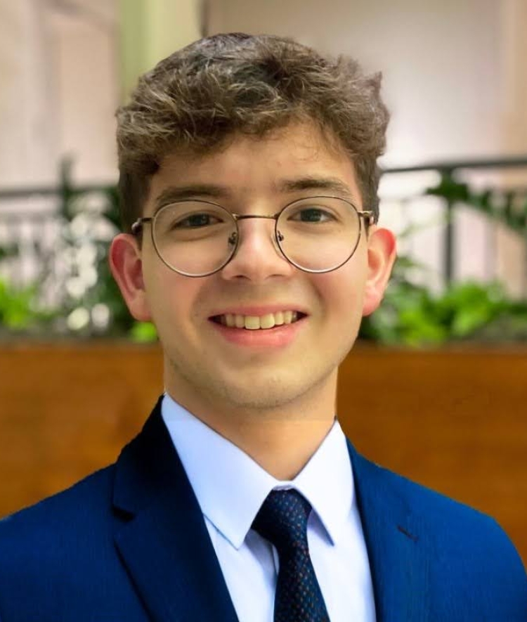 a young man wearing a suit and tie with glasses smiling