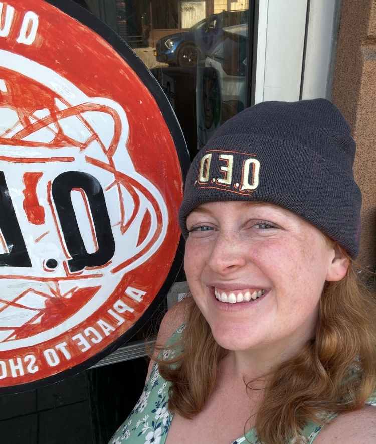 Hannah Lieberman '18 smiles next to a sign, wearing an embroidered QED beanie