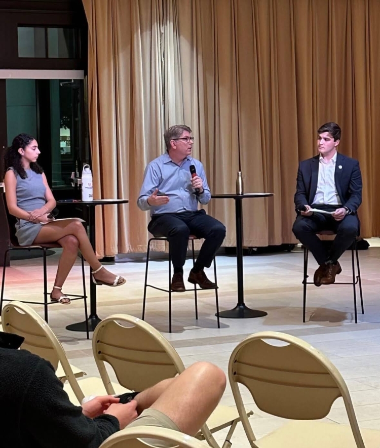 two students in business attire speak with a college president in front of an audience