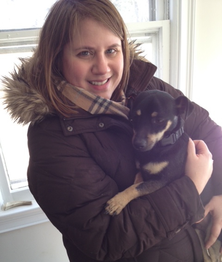 A smiling woman with brown hair and a puffy winter coat holds a small black and brown dog