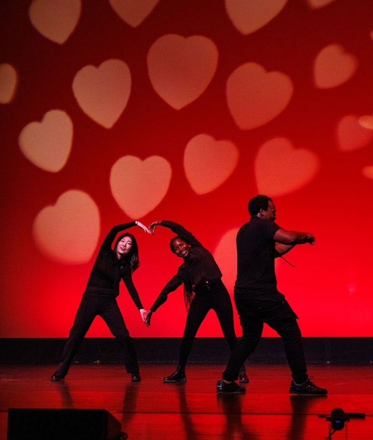young women form a heart with their arms while dancing on stage