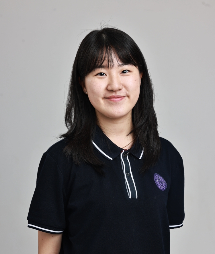 A young woman with dark hair and bangs smiles in a professional headshot while wearing a dark polo shirt with white trim.