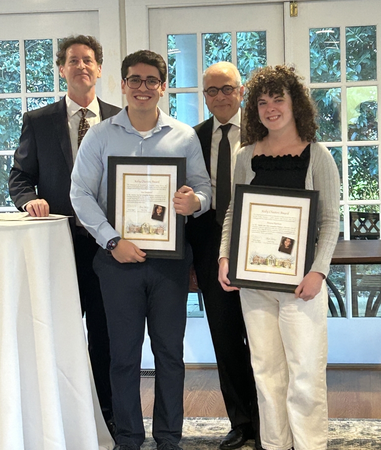 Two students smile while holding framed "Kathy Chaston Award" certificates, flanked by two faculty members in suits in an indoor setting with French doors.