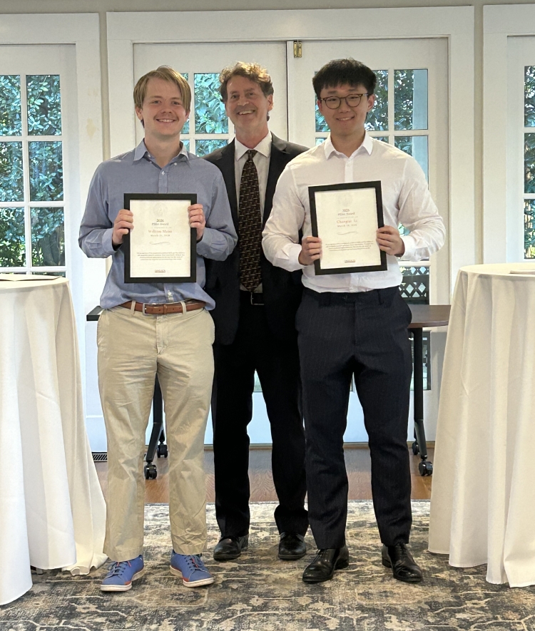 Two students stand together holding framed "2026 Pfifer Award" certificates, with a faculty member standing between them in the background.