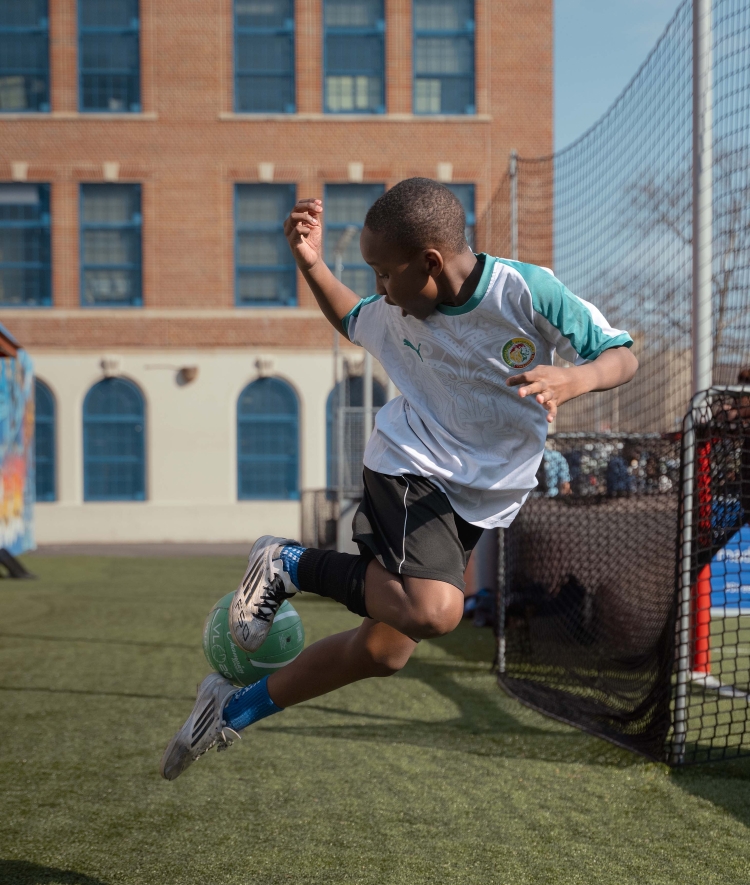 A boy in a soccer jersey does a cool aerial trick with a green soccer ball 