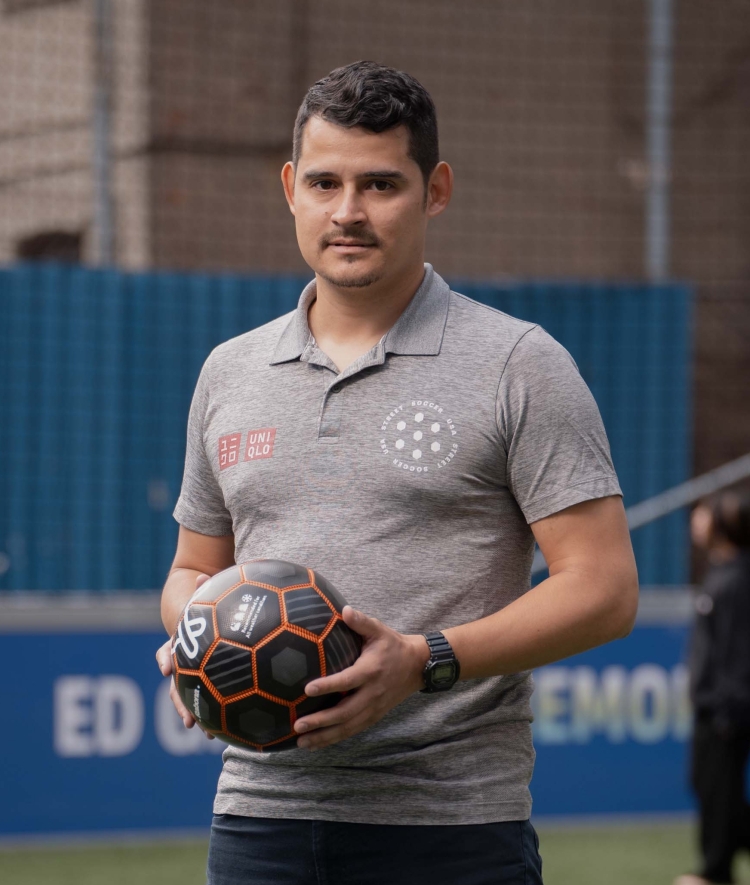 A man with dark hair and a mustache holds a black soccer ball