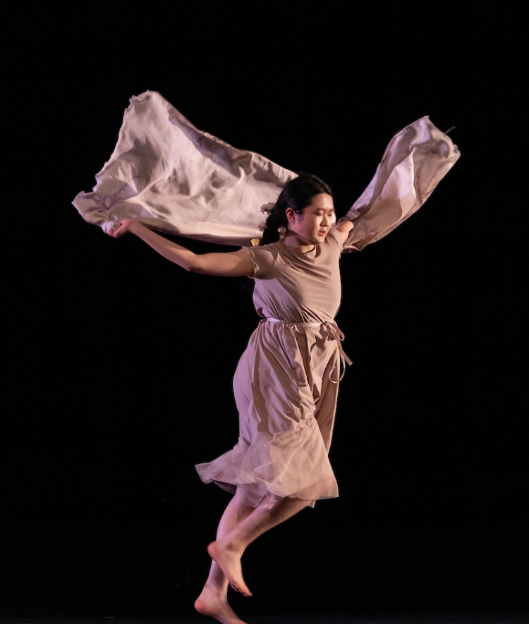 A student with long beige sleeves and a flowy dress dances onstage