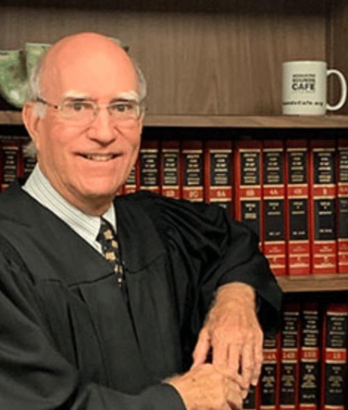 man standing in judge robes in front of bookcase