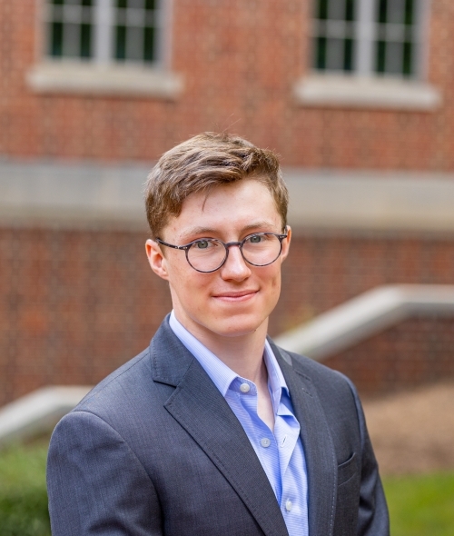 A student with short brown hair and glasses smiling