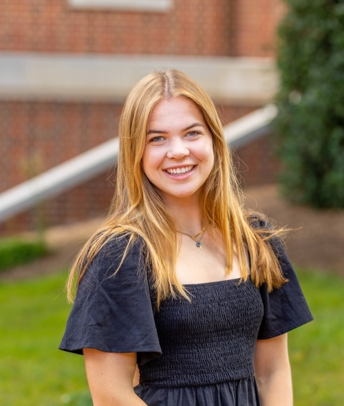 A young blonde woman wears a black dress and smiles