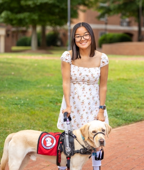 A young Asian woman smiles while holding the leash on her service dog