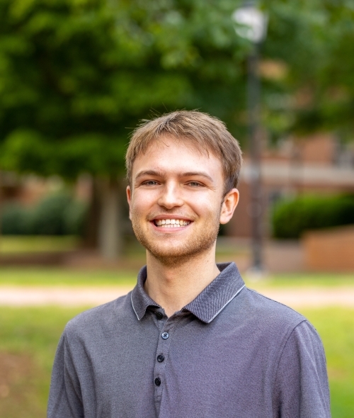 A young man with brown hair wears a blue collar and smiles