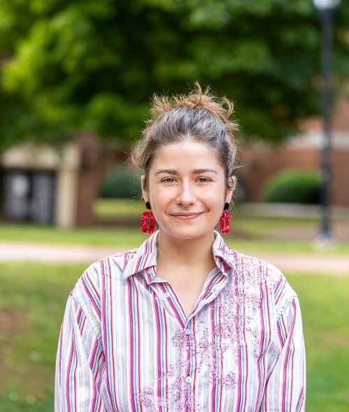 A white female with brown hair in a bun, wearing a striped shirt and red earrings