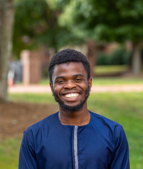 A young Black man wears a blue top and smiles