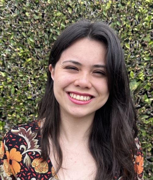 a young woman with dark brown hair wearing a floral top and smiling