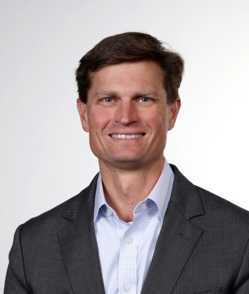 a young white man with brown hair wearing a jacket and smiling