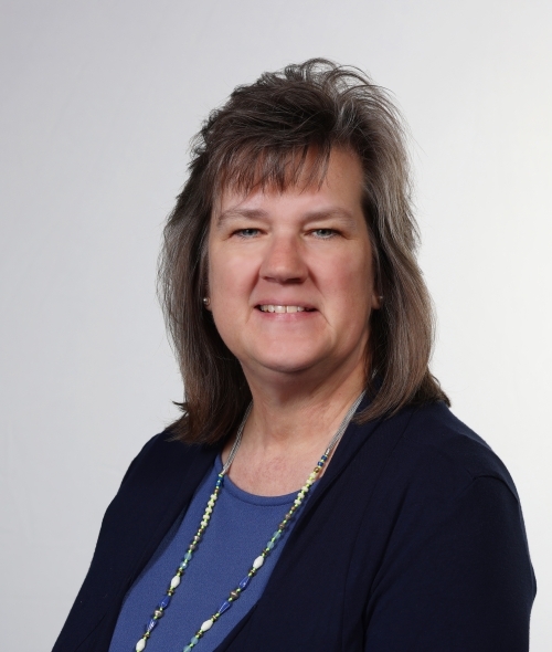 a middle aged white woman wearing a blue top and black jacket smiling
