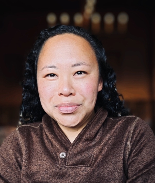 a young woman with black hair wearing a brown sweatshirt and smiling