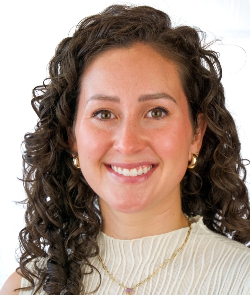 a young white woman with brown hair wearing a white top and gold necklace