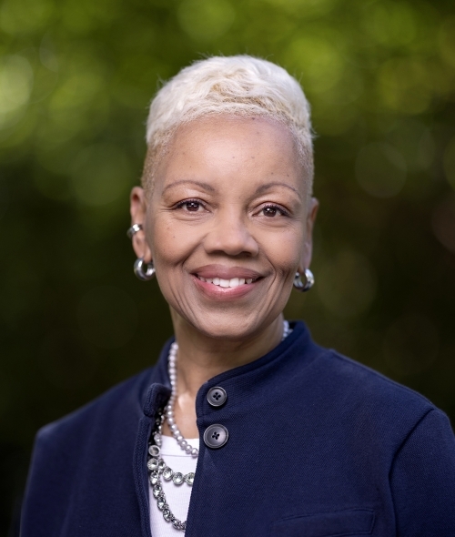 a middle aged Black woman with white hair wearing a blue jacket and hoop earrings