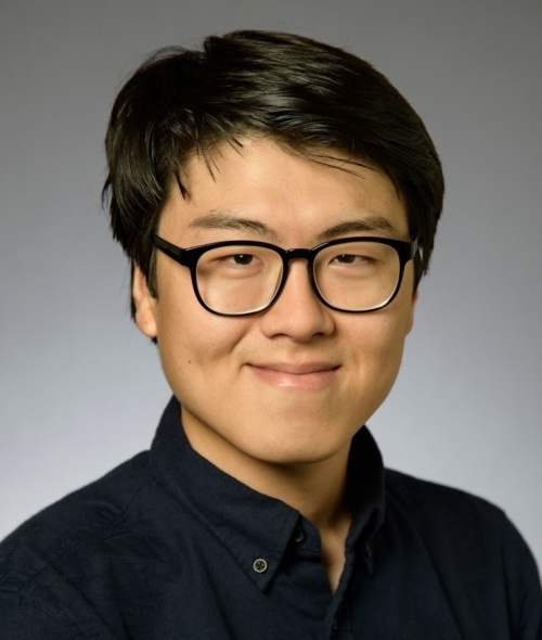 a young Asian male wearing a black shirt and glasses smiling