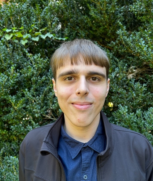 a young white man standing in front of greenery outside