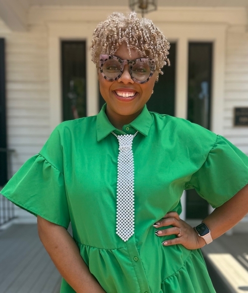 a young Black woman wearing a green dress and tie with glasses