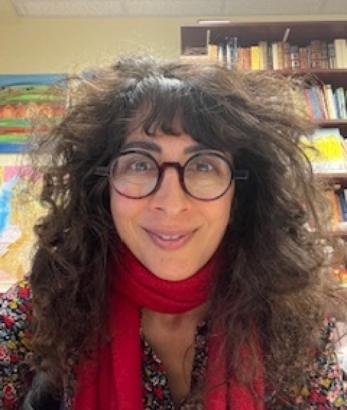 a middle aged white woman with curly brown hair wearing glasses and a red scarf