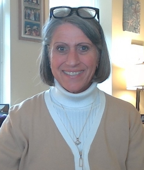 a white woman with grey hair wearing a white turtleneck and black glasses