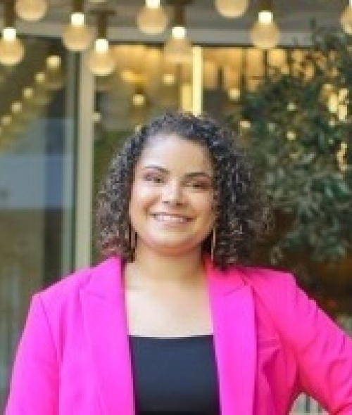 a young woman wearing a pink blazer with curly dark hair