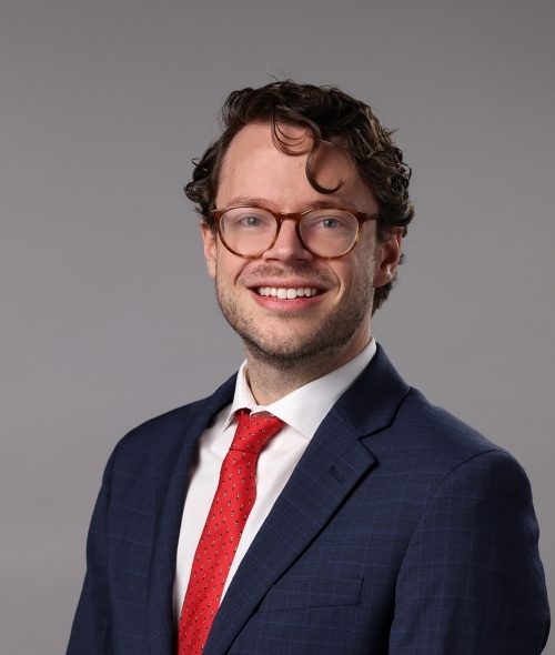 a young white man wearing glasses and a suit and tie with curly hair
