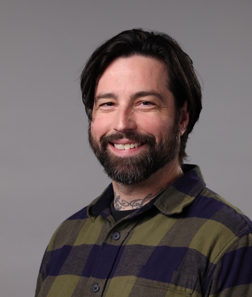 a man with brown hair and facial hair wearing a plaid shirt in a photo studio