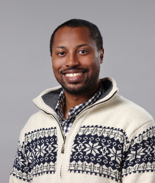 A young black man with facial hair wearing a white and navy blue knitted sweater