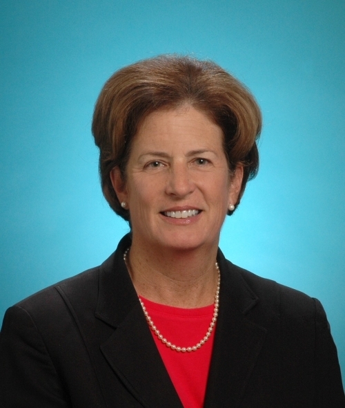 a middle aged white woman with short brown hair wearing a black blazer and red top