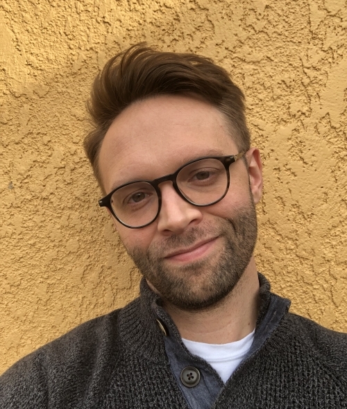 a young man wearing glasses and a grey sweater with short brown hair