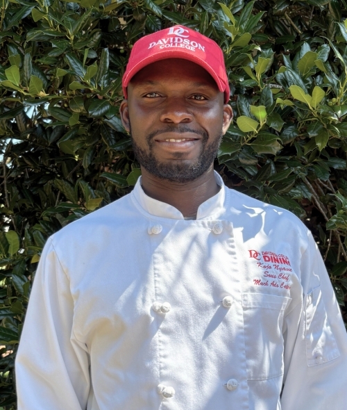 a young Black man wearing a chef's coat and red hat