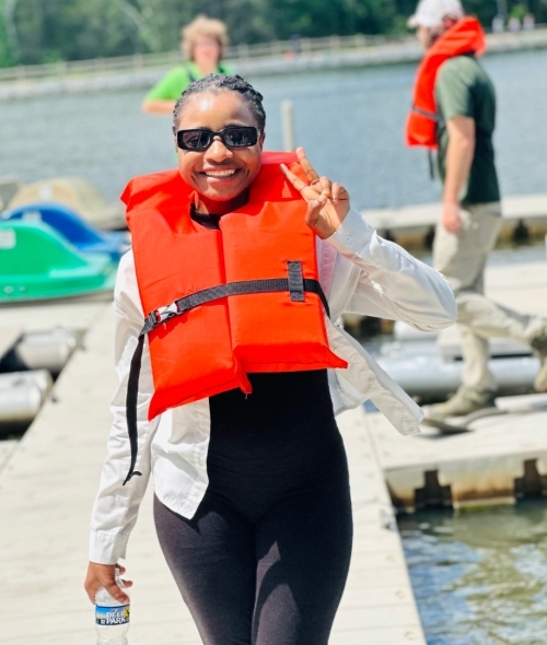 a young woman wearing a life jacket on a dock and smiling giving a peace sign