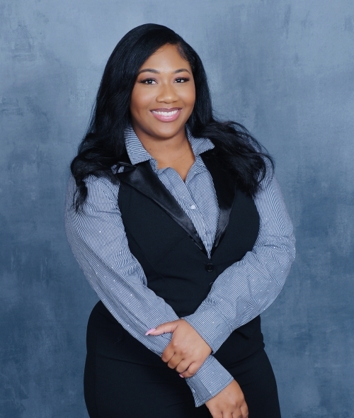 a young Black woman wearing a collared dress shirt and vest in front of a blue background