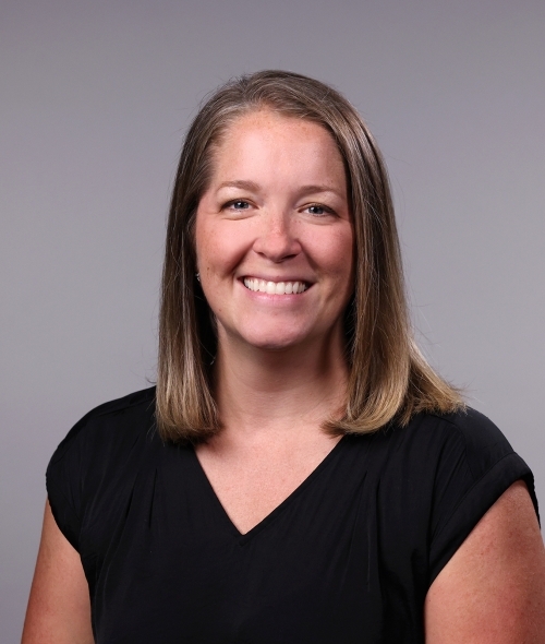 a woman with short dirty blonde hair wearing a black blouse on a grey background
