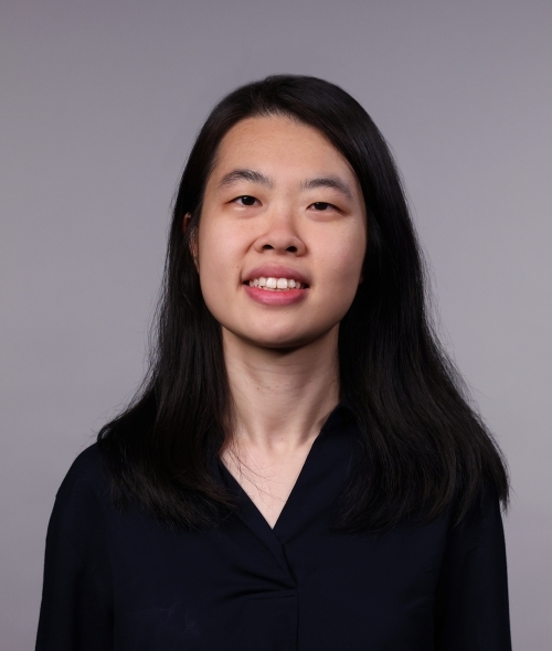 a woman with long black hair wearing a black blouse smiling on a grey background