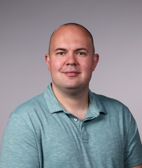 a man wearing an aqua polo smiling on a grey background