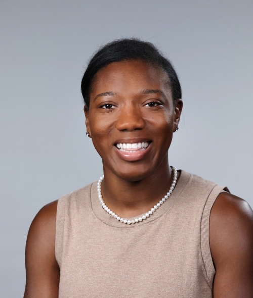 a woman with short black hair wearing a beige sweater top smiling on a grey background