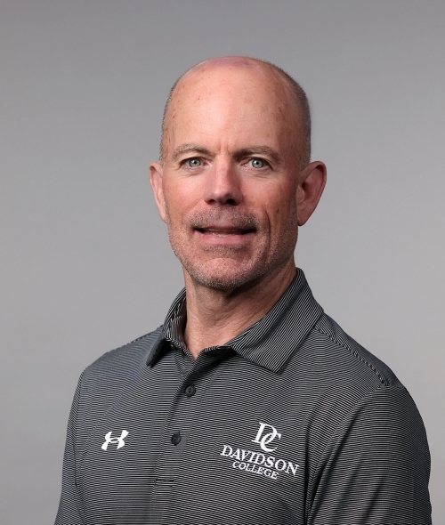 a white man wearing a grey golf shirt on a grey background