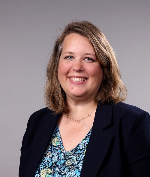 a woman with blonde hair wearing a blue blouse and black blazer on a grey background