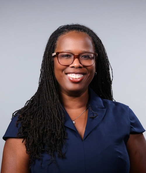 a woman with black hair wearing a navy blouse and red glasses on a grey background